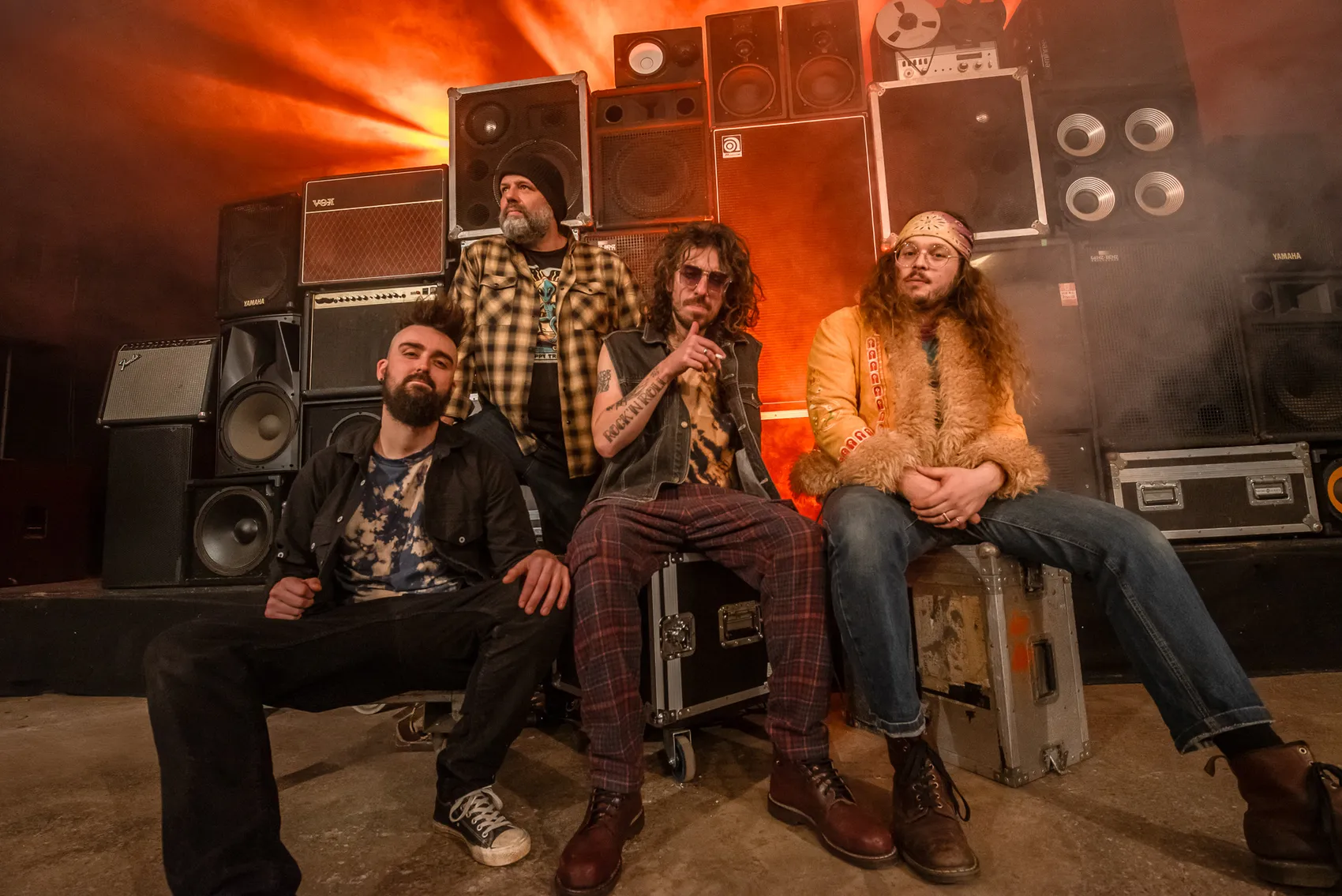 Vier Musiker der Band Trip posieren vor großen Lautsprecherboxen und Verstärkern im orangefarbenen Licht des iRock-Festivals 2026.