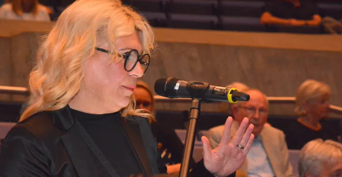 Zdenka Schwabauer spricht mit erhobener Hand in ein Mikrofon während einer öffentlichen Veranstaltung.