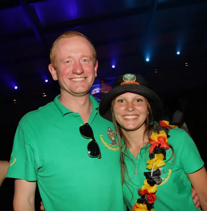 Ein Mann und eine Frau lächeln in die Kamera. Beide tragen grüne Poloshirts mit dem Logo der Landjugend Breckerfeld und eine Deutschlandflagge als Kette.