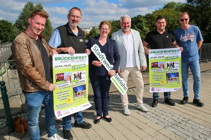 Sechs Personen präsentieren auf der Lennebrücke ein Programmplakat für das Brückenfest und ein Schild der Stadtwerke Iserlohn.