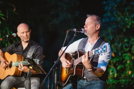 Tobias Janssen und George Schneider spielen akustische Gitarren und singen bei einem Live-Auftritt.