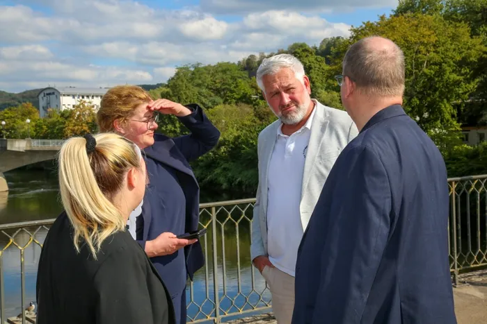 Chantal Kleine und Lutz Borgolte stehen im Gespräch mit anderen Personen an einem Geländer an einem Fluss.