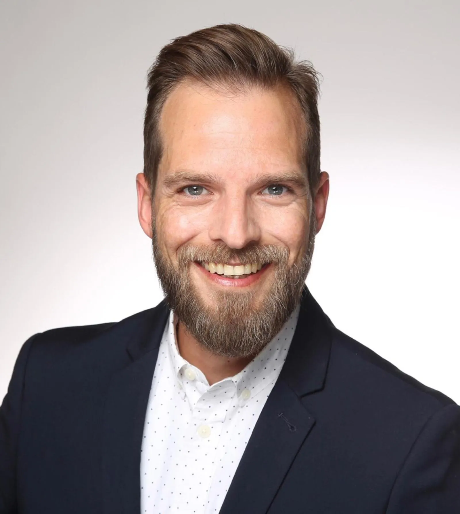 Porträt von Jens Willkens, SPD-Kandidat für Menden, mit Bart und im Anzug lächelnd in die Kamera.
