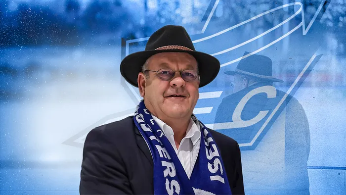 Porträt von Josef Jost mit Hut und Schal des Iserlohner EC, im Hintergrund verschwommenes Teamlogo und Spielerabbildung.