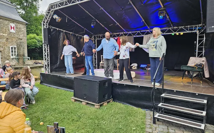 Sechs Personen tanzen Hand in Hand auf einer Bühne vor Publikum. Im Hintergrund ein Schloss und Bäume.