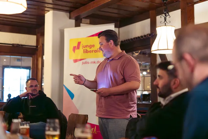 Justus Hein spricht vor Anwesenden in einem Gastraum, im Hintergrund ein Banner mit dem Logo der Jungen Liberalen und der Aufschrift „junge liberale“.