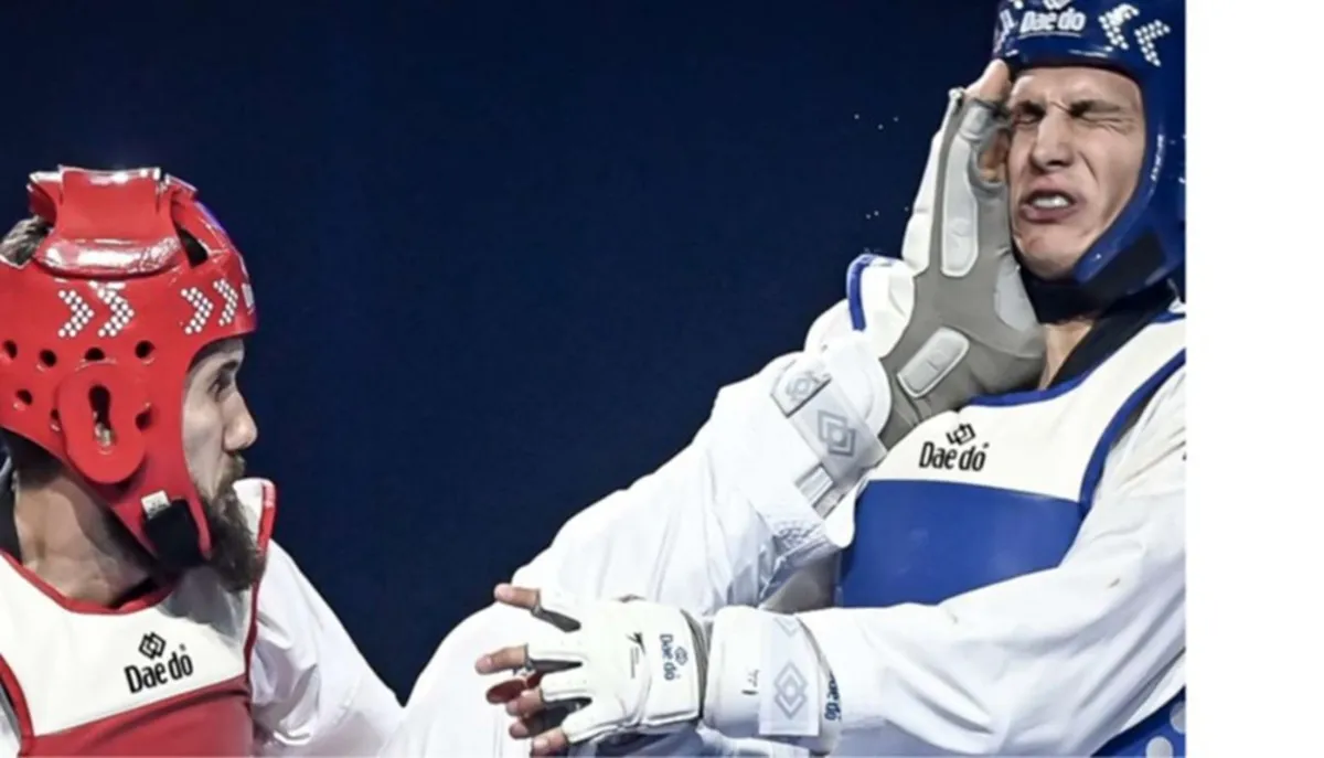 Zwei Taekwondo-Athleten im Kampf: Links ein Kämpfer mit rotem Kopfschutz, rechts ein Kämpfer mit blauem Kopfschutz, der einen Tritt ausführt.