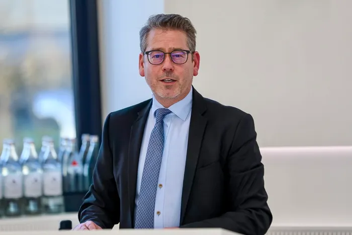 Karsten Meininghaus mit Brille, dunklem Anzug und blau gemusterter Krawatte blickt in die Kamera.