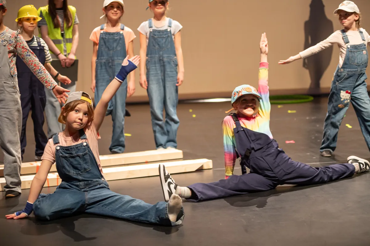 Zwei Kinder in Latzhosen und Mützen deuten beim Auftritt auf einer Bühne mit weiteren Kindern im Hintergrund die Arme nach oben. Die Show „Kaskadia“ feierte am Freitagabend Premiere.