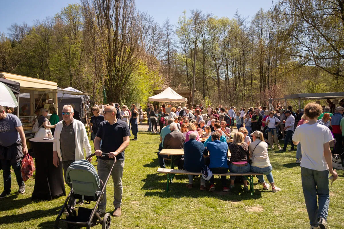 Viele Menschen genießen das Frühlingsfest auf der grünen Wiese vor der Heesfelder Mühle, einige sitzen an Biertischen und essen oder unterhalten sich.