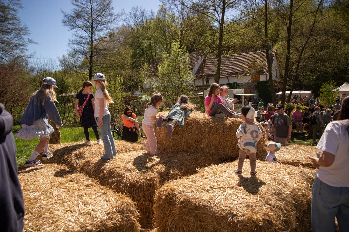 Kinder spielen und klettern auf Heuballen vor einer historischen Mühle bei einem Frühlingsfest.