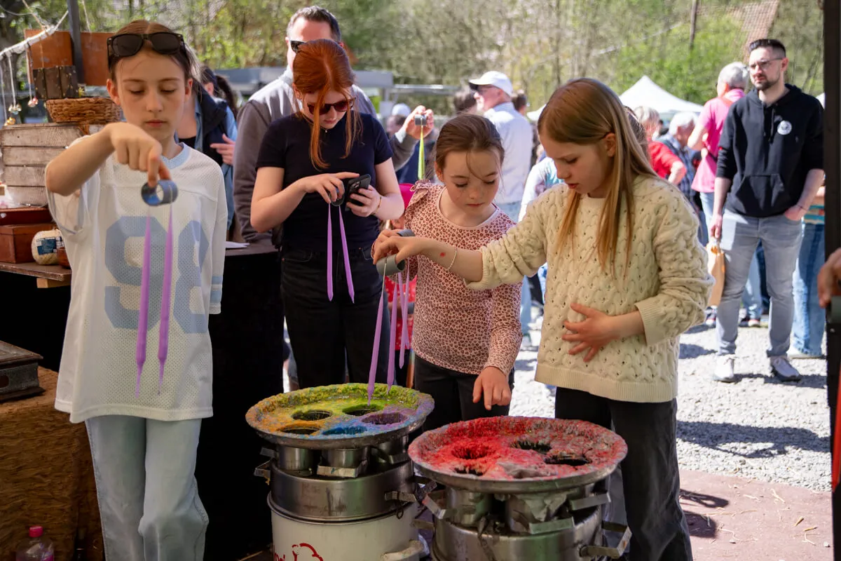 Kinder tauchen bunte Wachsstäbchen in farbige Wachstöpfe auf dem Kirschblütenfest an der Heesfelder Mühle.