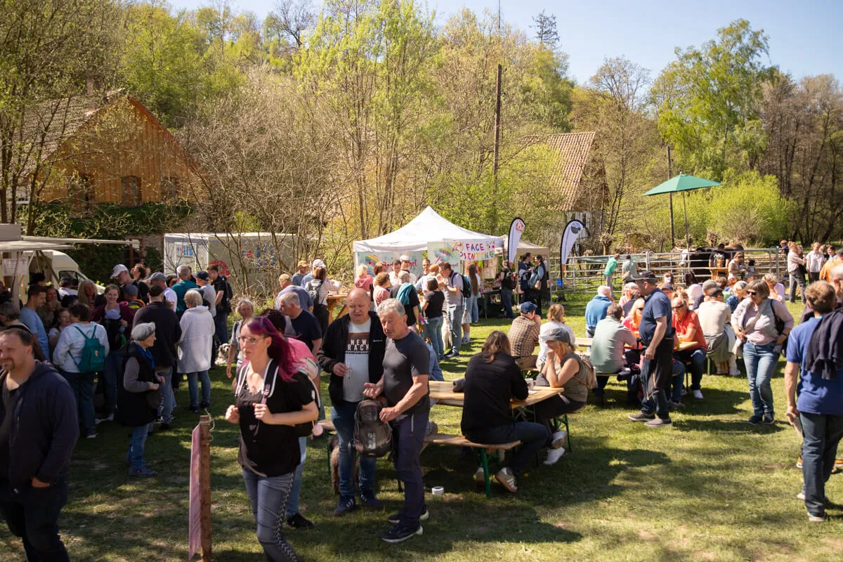 Volksfest mit vielen Besuchern an Biertischen und Buden vor ländlichem Hintergrund.