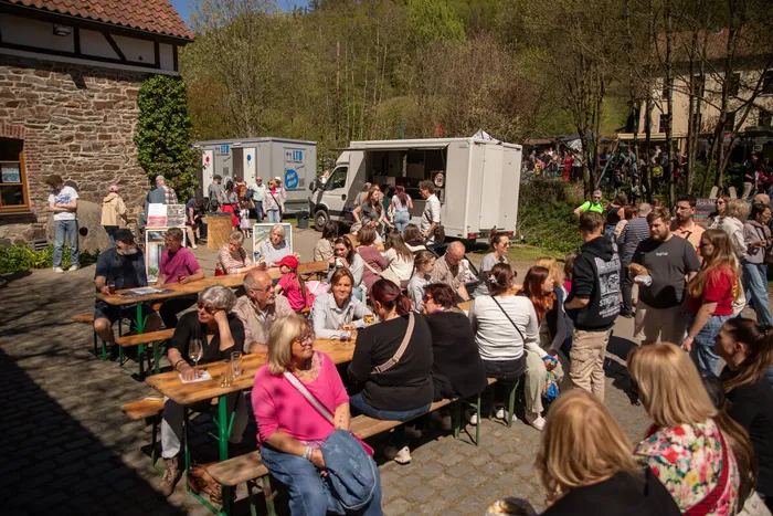 Menschen sitzen an Biertischgarnituren vor einer Fachwerkmühle und genießen Getränke und Gespräche bei einem Frühlingsfest.