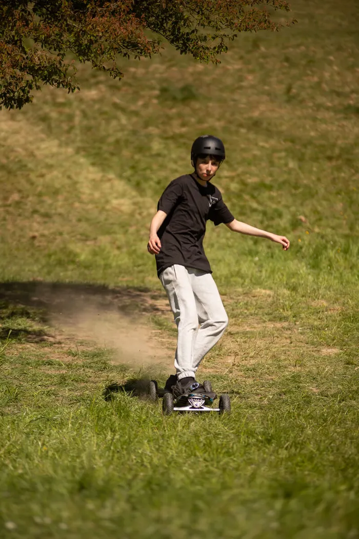 Ein Jugendlicher fährt mit einem elektrischen Skateboard auf einer Wiese, trägt einen Helm und lockere Kleidung.