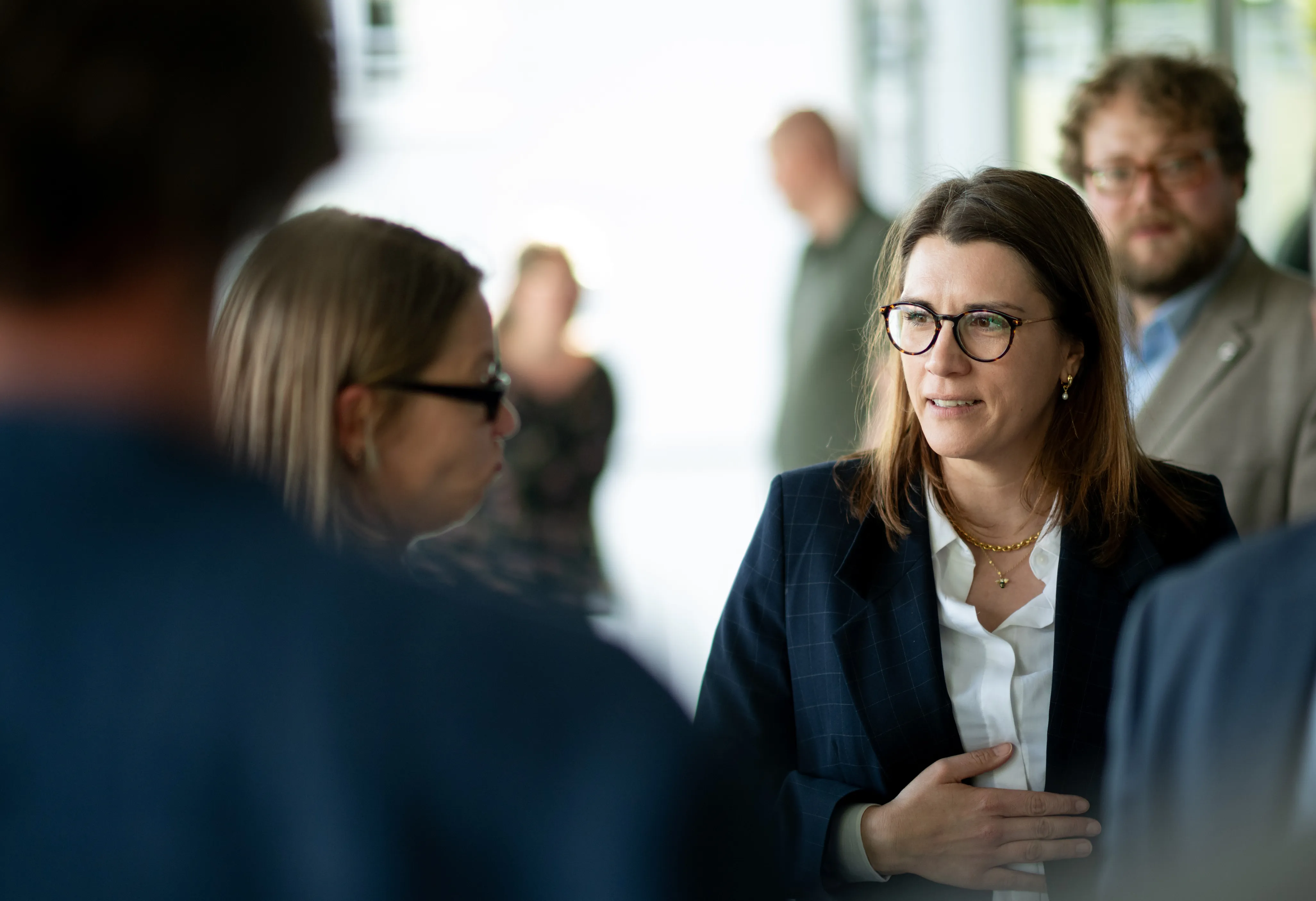 Ina Blumenthal, eine Frau mit Brille und Blazer, spricht auf einem Gipfel mit einer anderen Frau. Im Hintergrund sind weitere Personen zu sehen.