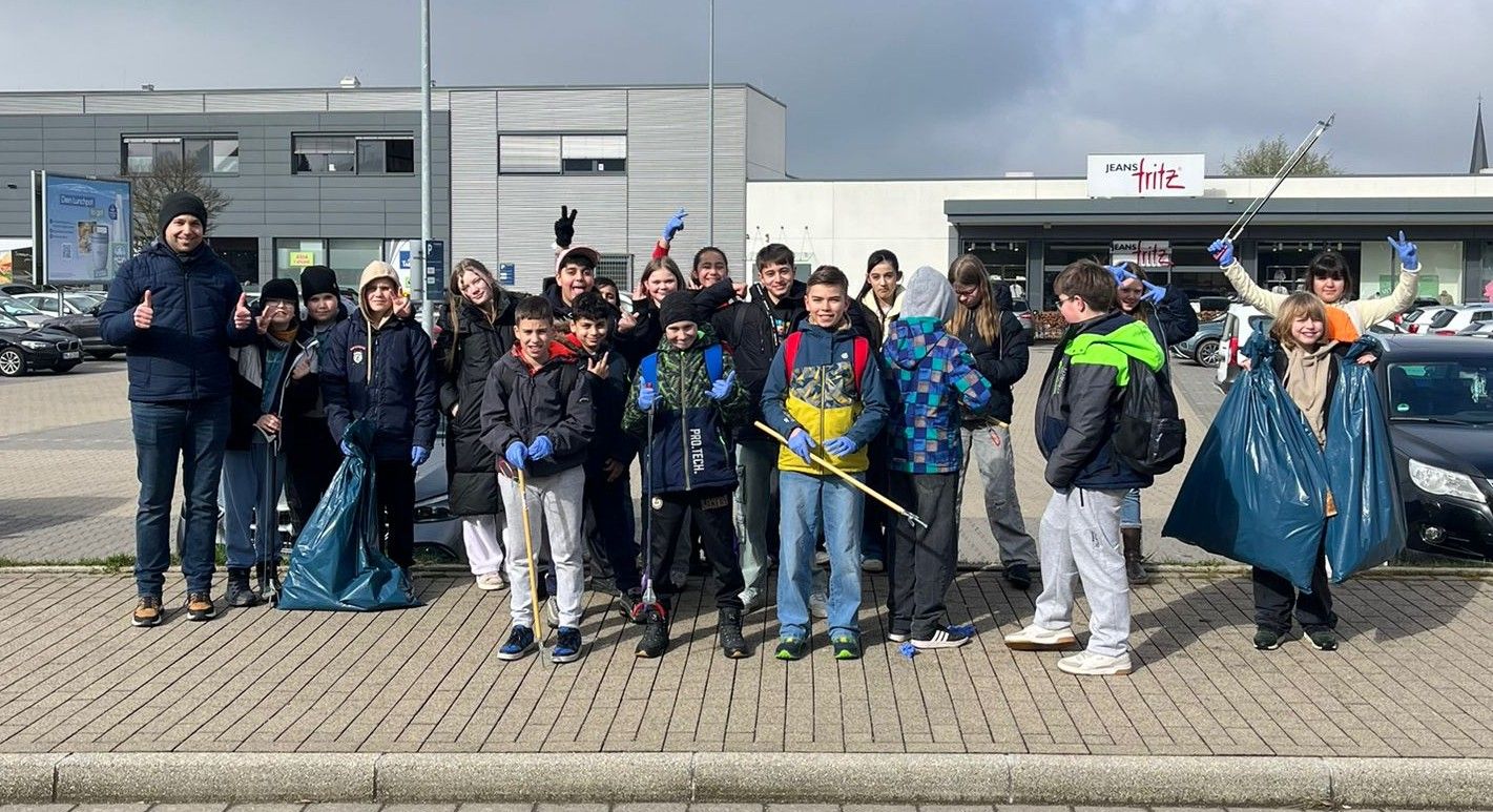 Eine Gruppe von Schülerinnen und Schülern der fünften und sechsten Klassen der Humboldtschule steht mit Müllsäcken und Greifwerkzeugen vor einem Geschäft in Halver. Sie haben an einer Müllsammelaktion teilgenommen.