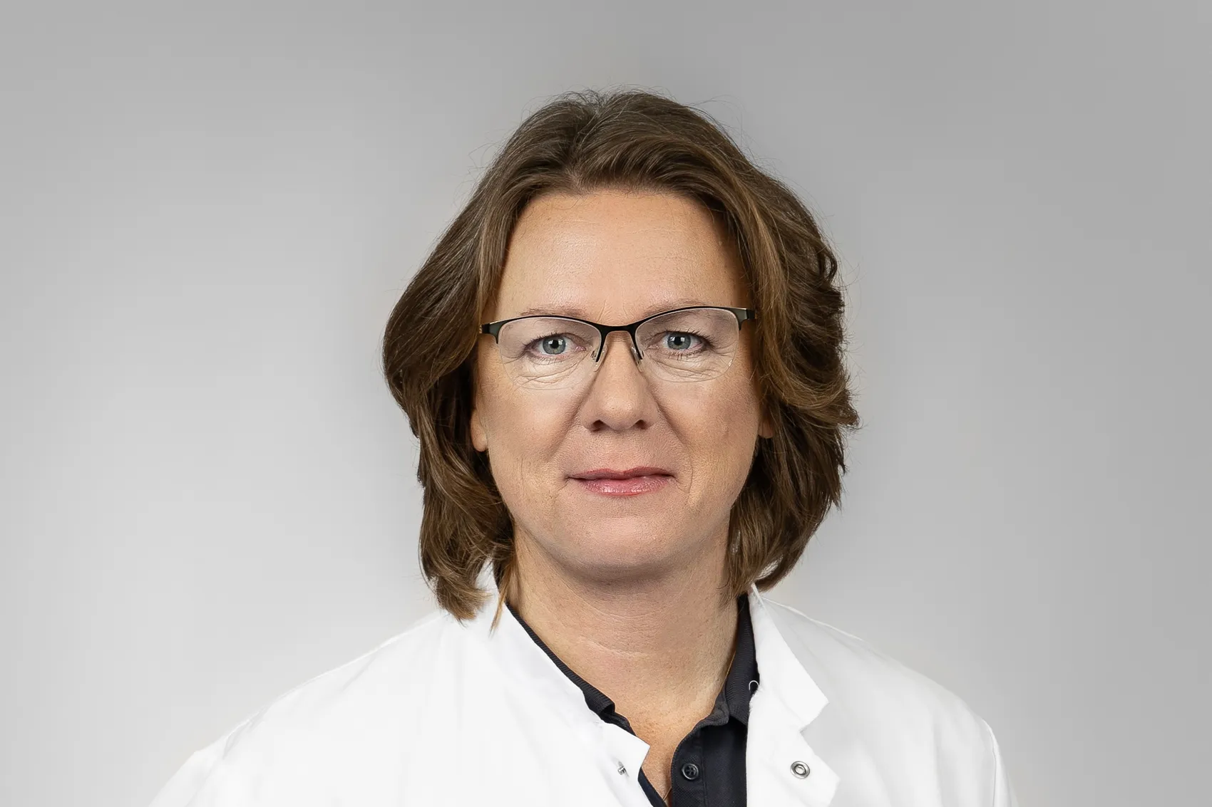 Porträt von Andrea Knichel, einer Frau mit braunem Haar und Brille, die einen weißen Kittel trägt.