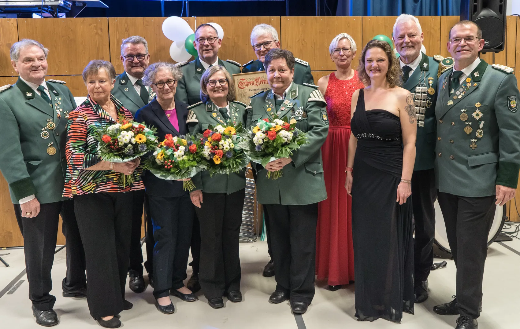 Gruppe von etwa zehn Personen in festlicher Kleidung, darunter mehrere in grünen Uniformen mit Orden, posiert mit Blumensträußen auf einem Königsball.