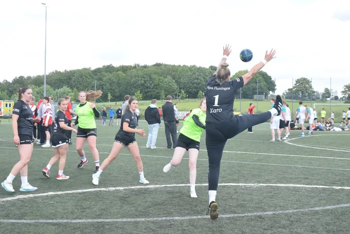 Eine Spielerin des Teams „Flamingos“ wirft im Handballspiel den Ball ab. Im Hintergrund sind weitere Spielerinnen und Zuschauer auf dem Sportplatz zu sehen.