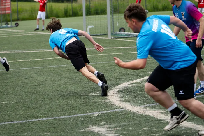 Ein Fußballspieler in einem blauen Trikot mit der Nummer 10 sprintet auf dem grünen Kunstrasen. Im Hintergrund stürzt ein anderer Spieler, während weitere Personen im Hintergrund stehen.