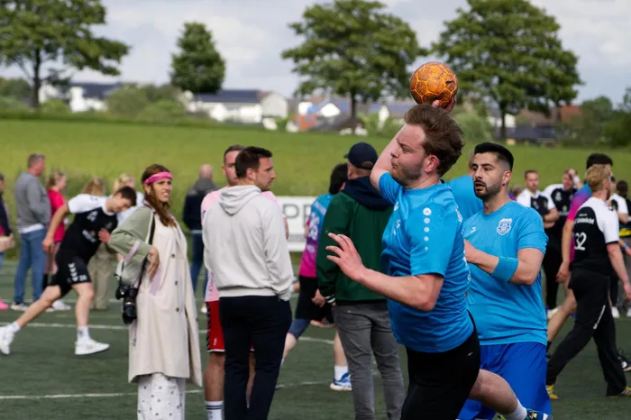 Ein Fußballspieler in blauem Trikot köpft den Ball während eines Spiels auf einem grünen Rasenplatz. Im Hintergrund sind weitere Spieler und Zuschauer zu sehen.
