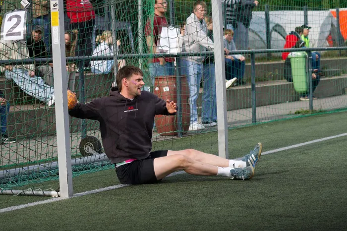 Ein Mann kniet auf dem Spielfeld vor einem Handballtor und jubelt mit geballter Faust. Im Hintergrund stehen und sitzen Zuschauerinnen und Zuschauer.
