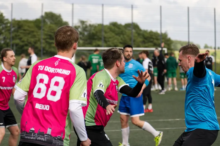 Fußballspieler in pinken und blauen Trikots feiern auf dem Spielfeld, während andere Spieler im Hintergrund stehen. Einer der Spieler trägt die Nummer 68 und den Namen „Benjo“ auf dem Rücken.