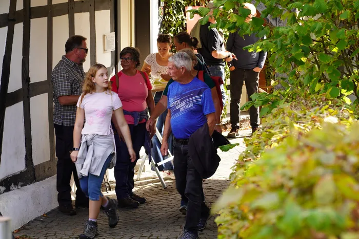 Eine Gruppe von Wanderern geht auf einem gepflasterten Weg an einem Fachwerkhaus vorbei.
