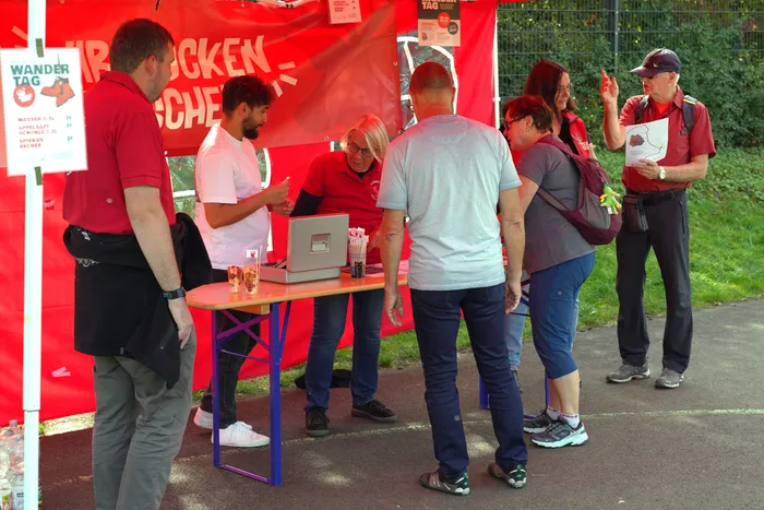 Menschen an einem Stand unter einem roten Zelt bei einer kulinarischen Wanderung in Herscheid.