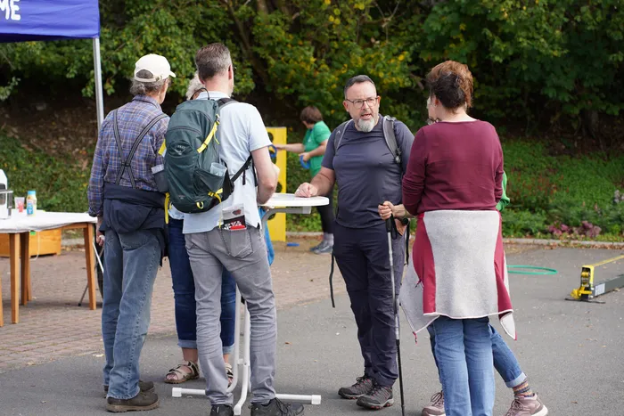 Eine Gruppe von Wanderern mit Rucksäcken und Wanderstöcken steht im Freien um einen Tisch.