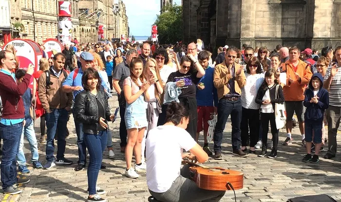 Ein Straßenmusiker spielt Gitarre auf einem Kopfsteinpflaster vor einer Zuschauermenge beim Fringe Festival in Edinburgh.