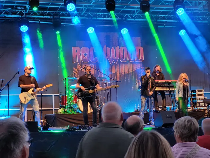 Die Coverband Rockwood tritt auf einer Bühne mit blauem und grünem Scheinwerferlicht vor einem Publikum auf.