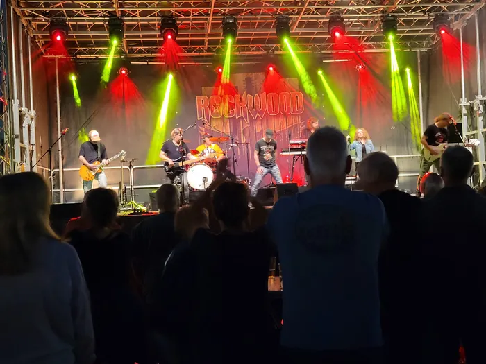 Die Band Rockwood spielt auf einer Bühne unter roter und grüner Scheinwerferbeleuchtung vor einem Publikum.