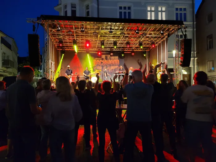 Die Band Rockwood spielt auf einer farbig beleuchteten Bühne vor einem Publikum mit erhobenen Händen.