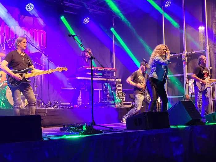 Die Coverband Rockwood tritt live auf einer Bühne unter violettem und grünem Licht auf.