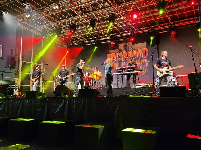 Die Coverband Rockwood tritt auf einer Bühne mit farbigen Scheinwerfern und dem Schriftzug „ROCKWOOD“ im Hintergrund auf.