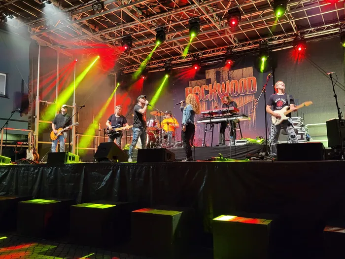 Die Coverband Rockwood spielt auf einer Bühne mit farbenfroher rot-gelb-grüner Beleuchtung vor einem großen „Rockwood“-Schriftzug.