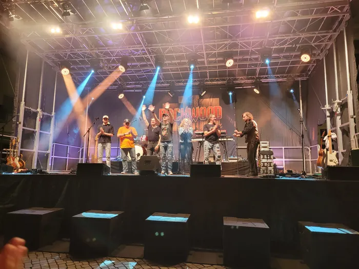 Die Mitglieder der Coverband Rockwood stehen nebeneinander auf einer Bühne unter hellen Scheinwerfern.