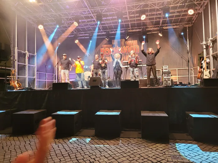 Die Coverband Rockwood performt auf einer Bühne unter hellen Scheinwerfern mit dem Schriftzug „ROCKWOOD“ im Hintergrund.