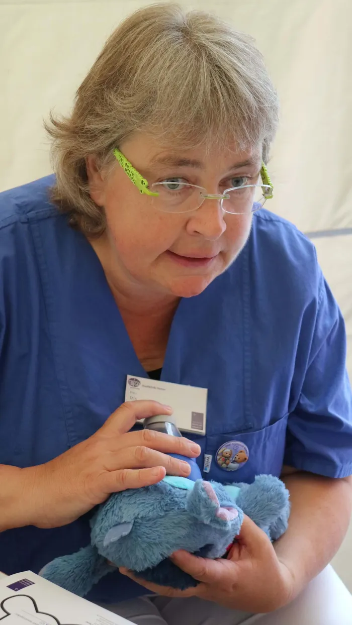 Eine Frau in blauer medizinischer Kleidung hält ein blaues Kuscheltier in den Händen.