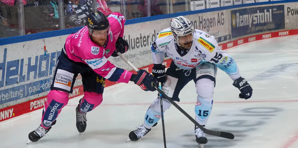 Zwei Eishockeyspieler im Zweikampf: Kyle Wood (Iserlohn Roosters, rosa Trikot) und C.J. Suess (Dresdner Eislöwen, blau-weißes Trikot) während eines Spiels.