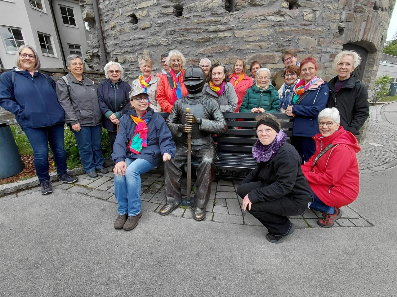Eine Gruppe von etwa zwanzig Frauen mittleren und höheren Alters posiert lächelnd vor einer Ritterstatue auf einer Bank vor einer alten Steinmauer.