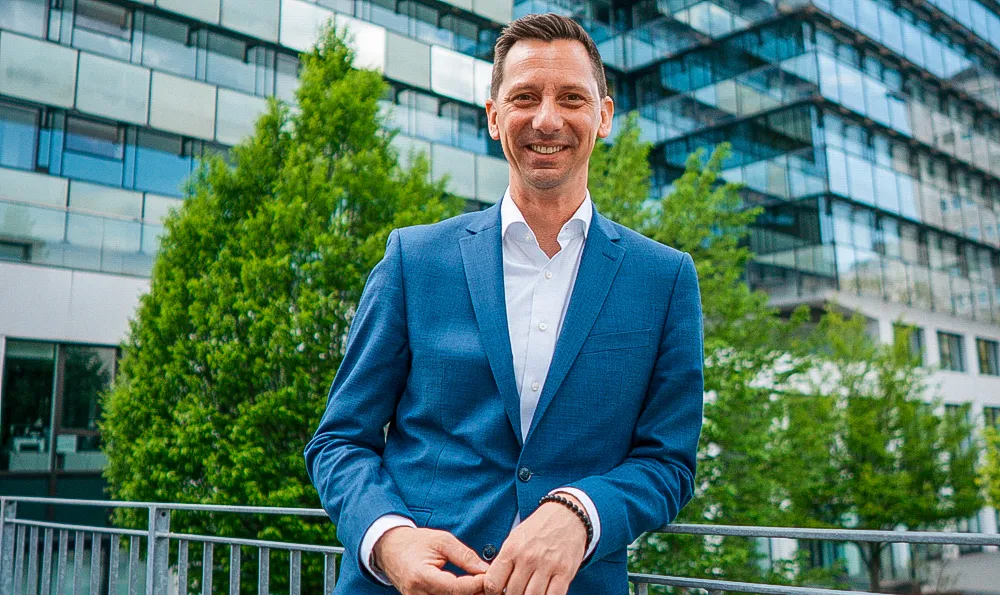 Landrat Andreas Müller lächelt in einem blauen Anzug vor dem modernen Glasgebäude des Kreishauses in Siegen.