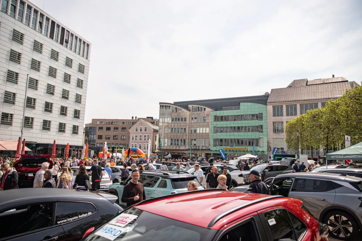 Menschenmengen und Autos füllen einen Stadtplatz an einem sonnigen Tag während des FIDLI-Festivals. Im Hintergrund sind moderne Gebäude und Geschäfte zu sehen.