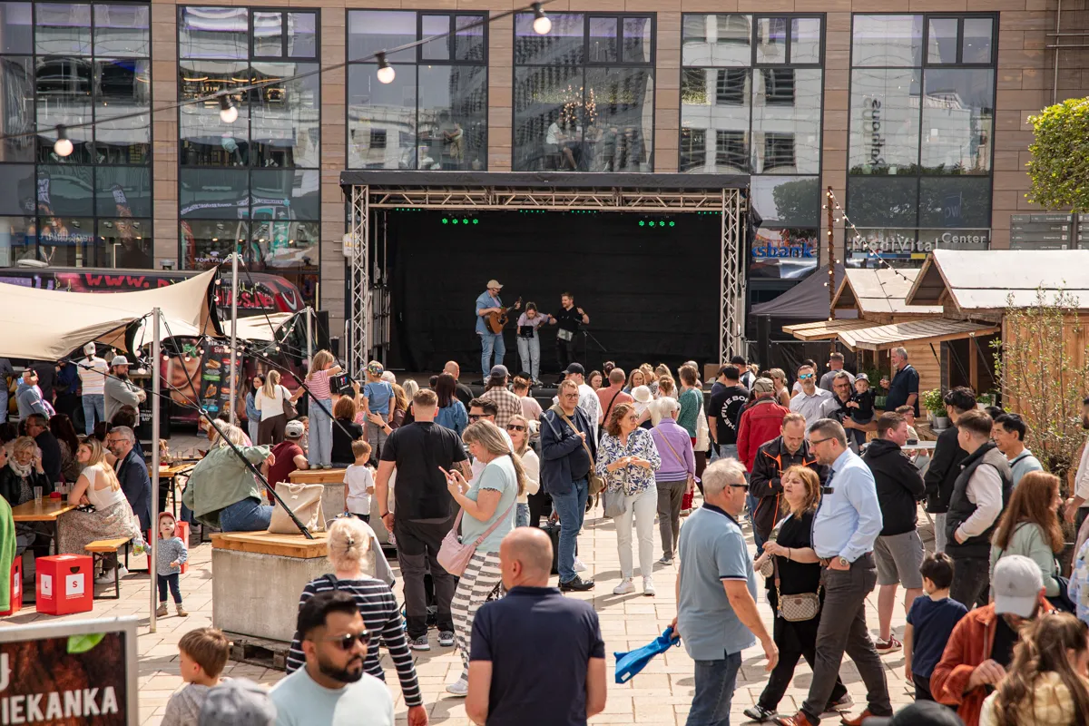 Volksfest mit Musikbühne und vielen Besuchern auf einem Stadtplatz. Im Hintergrund moderne Glasfassaden.