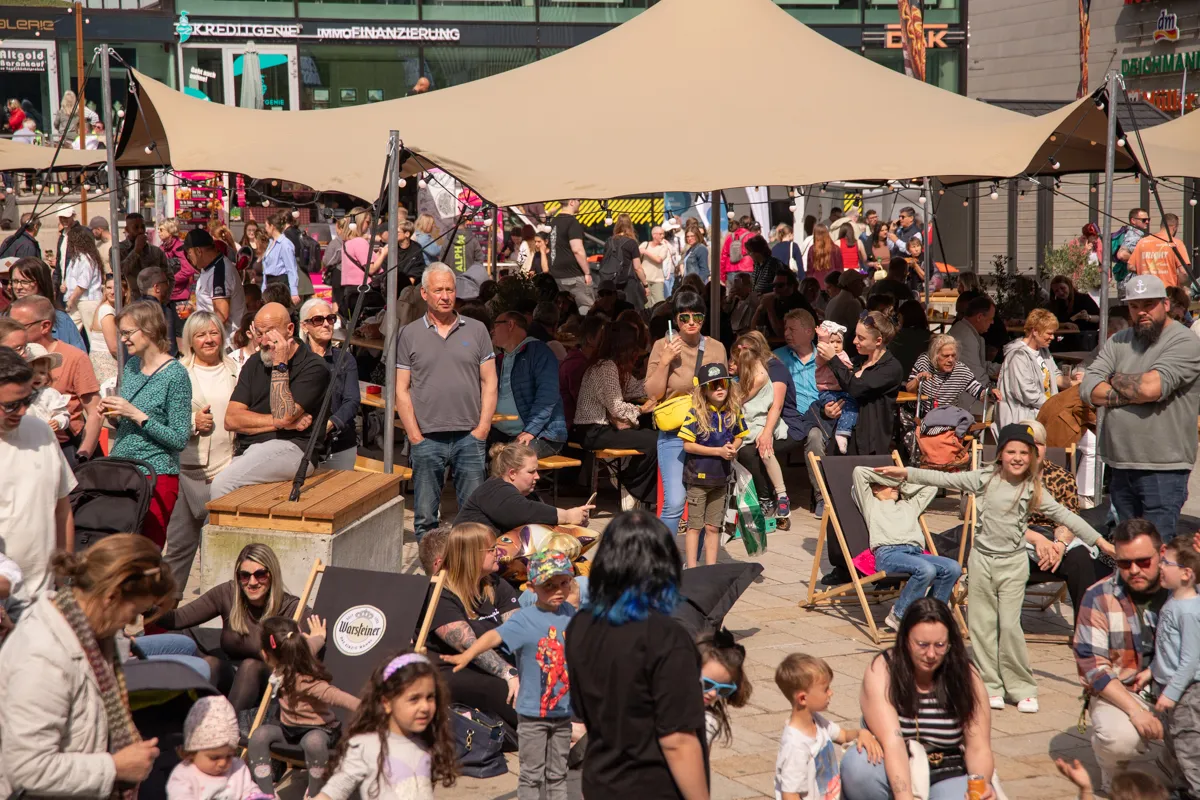 Menschen drängen sich auf einem belebten Platz in der Innenstadt, viele sitzen an Tischen und genießen das sonnige Wetter während des Frühlingfestes.