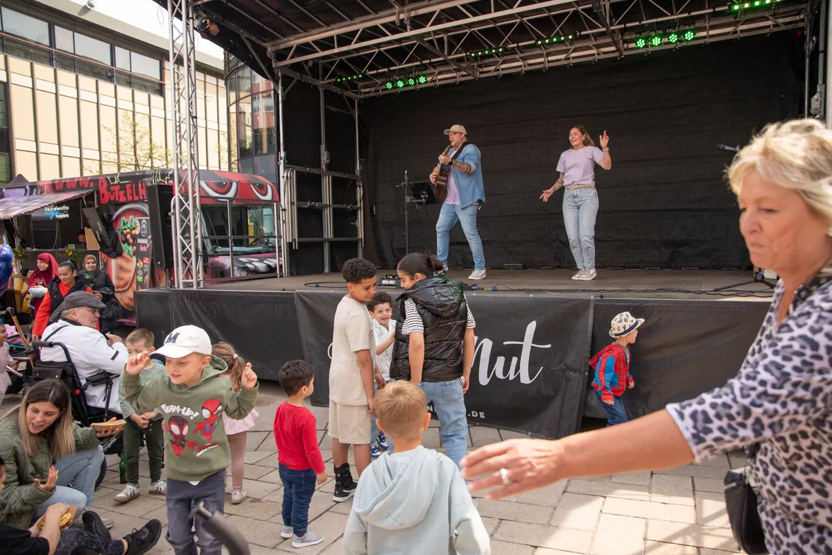 Ein Mann mit Gitarre und eine Frau singen auf einer Bühne vor einem Publikum aus Kindern und Erwachsenen im Rahmen des Stadtfestes Frühling in der Lüdenscheider Innenstadt.