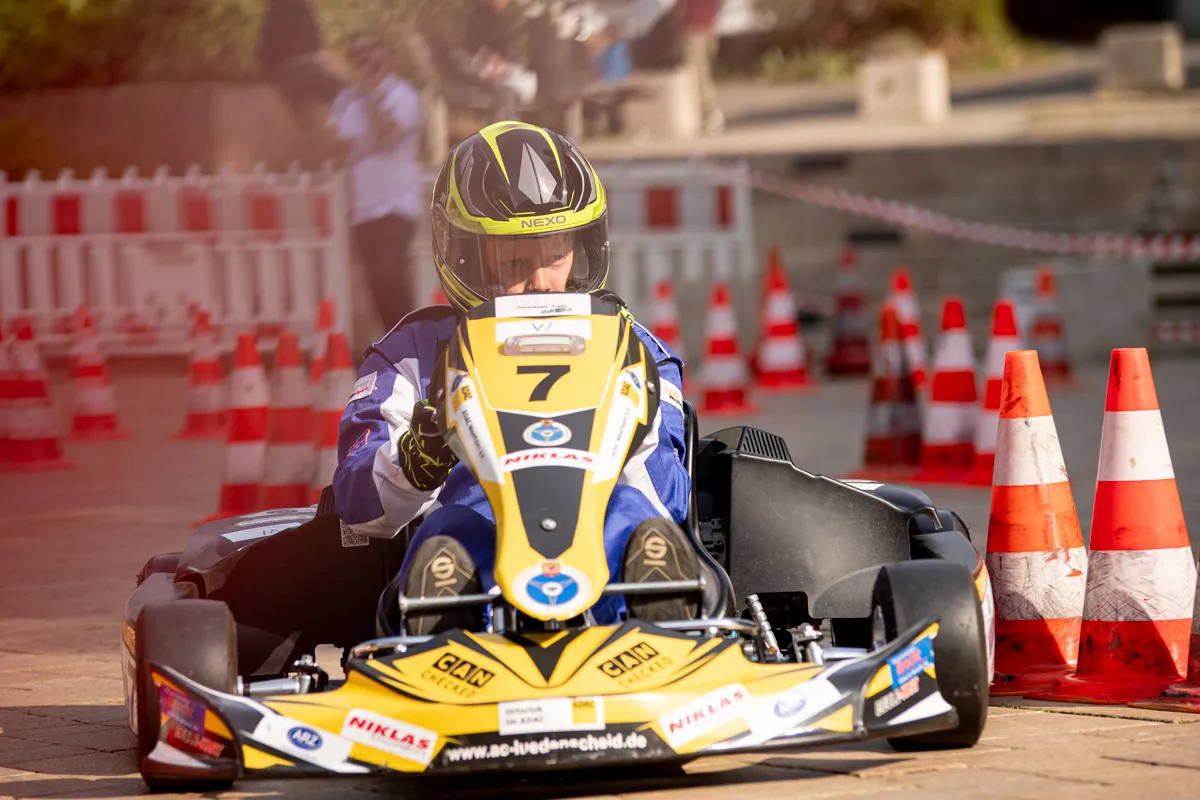Kartfahrer mit der Startnummer 7 fährt auf einer abgesperrten Strecke durch die Innenstadt, umgeben von orangefarbenen Pylonen und Absperrgitter.