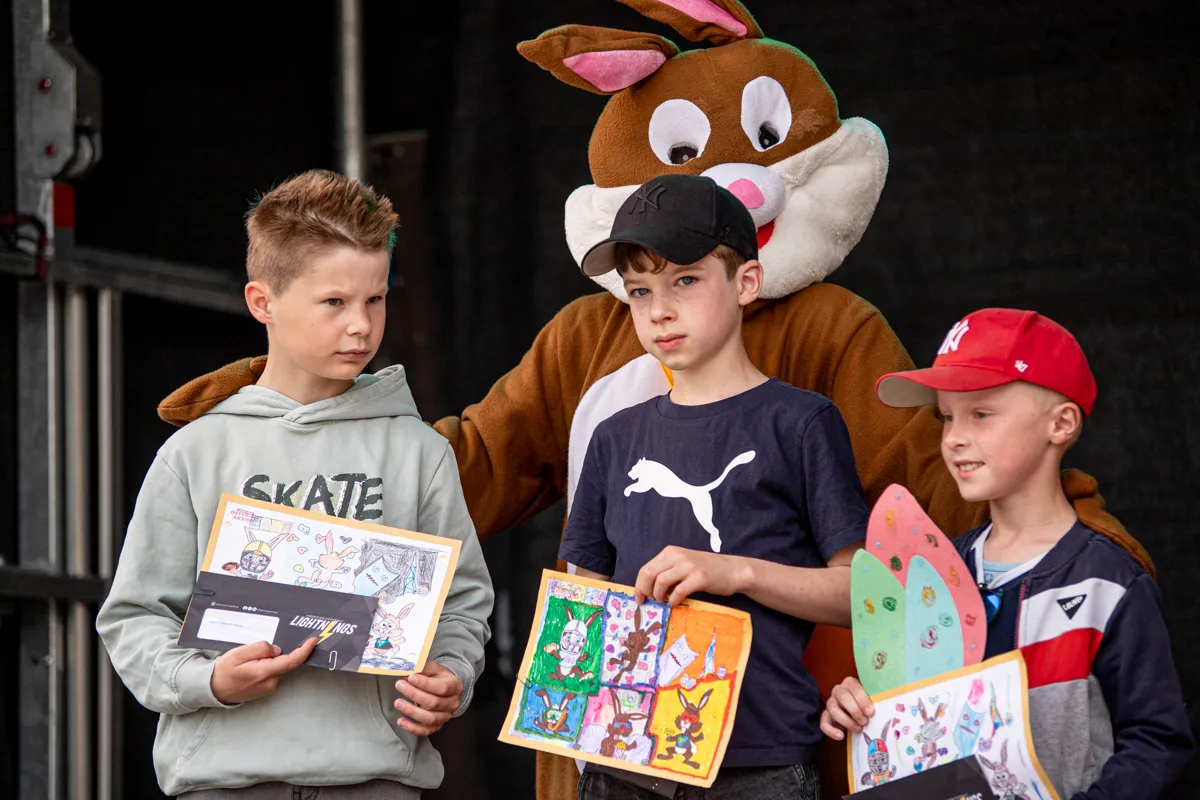 Drei Jungen halten bunte Bastelarbeiten mit Hasenmotiven vor sich. Im Hintergrund steht eine große Hasenfigur.